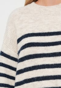 Pull beige clair en maille douce, avec des rayures horizontales bleu foncé et un col rond. Apparence texturée avec une coupe décontractée.