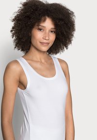 Camisola de alças larga branca de algodão com decote redondo, apresentando uma textura suave e um design ajustado.