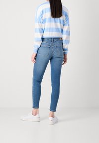 Jeans ajustados en denim azul claro con bolsillos traseros, combinados con una camiseta de rayas azul y blanca de manga larga y zapatillas blancas.