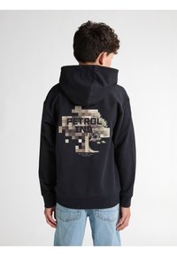 Felpa nera con una grande grafica pixelata di un albero sul retro. Il testo recita "PETROL IND." Il tessuto sembra morbido; polsini e orlo a coste.
