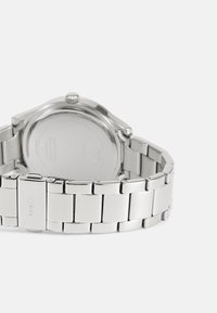 Srebrni metalni ručni sat s poliranim narukvicom, okruglim kućištem i minimalističkim dizajnom. Stražnja strana kućišta glatka je s detaljima o proizvodnji.