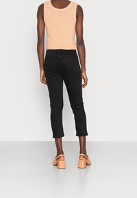 Jeans negros cortos con un ajuste slim, combinados con una camiseta sin mangas de canalé beige. La modelo lleva sandalias nude de tacón cuadrado. Diseño simple y minimalista.
