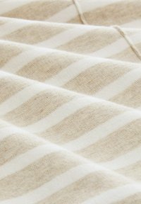 Baumwollstoff mit abwechselnd beigen und weißen diagonalen Streifen, die eine weiche, strukturierte Oberfläche aufweisen. Die Streifen erzeugen ein kontrastierendes Muster.