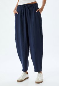 Lässig geschnittene navyblaue Hose aus weichem Stoff mit einem elastischen Bund und Seitentaschen, die eine entspannte Silhouette bietet.