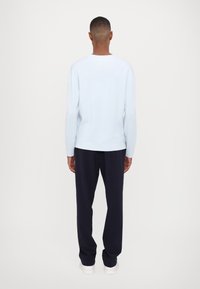 Jasnoniebieski sweter dziany z długimi rękawami, okrągłym dekoltem i prążkowaną fakturą, zestawiony z ciemnogranatowymi spodniami i białymi tenisówkami.