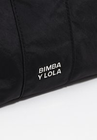 Borsa a spalla nera in tessuto con una superficie liscia, forma rettangolare e un logo bianco ben visibile con la scritta "BIMBA Y LOLA."