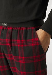Czarny longsleeve połączony z spodniami w kratę w odcieniach czerwieni i czerni. Spodnie mają elastyczny pas oraz boczne kieszenie. Miękka faktura materiału.
