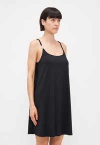 Vestido negro sin mangas de corte relajado, hecho de una tela suave. Las tirantes ajustables tienen un detalle plateado en un lado.