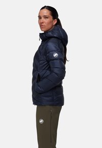 Marineblauwe gewatteerde jas met capuchon, met een gestructureerde afwerking, ritszakken en een logo op de linker mouw. Gepaard met olijfgroene broek.