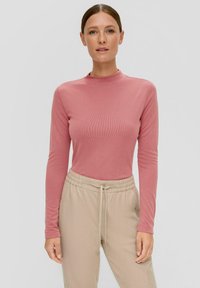 Haut à manches longues en tissu à rayures rose doux avec un col montant, associé à un pantalon beige à cordon de serrage. Texture lisse, design ajusté.
