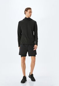 Sort langærmet træningstop med hætte, parret med sorte shorts. Begge beklædningsgenstande har en glat tekstur og er designet til aktivitet.