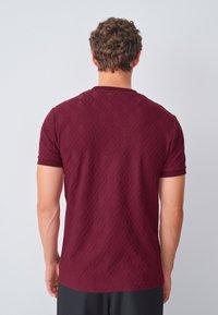 Maroon textured short-sleeve T-shirt with a patterned design, featuring a ribbed crew neckline and fit. Back view with no visible logo.