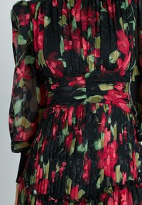 Zwarte jurk met een bloemenpatroon van rode en groene rozen. Gepleatste textuur met een gegatherde taille en rimpelranddetails. Lange mouwen.