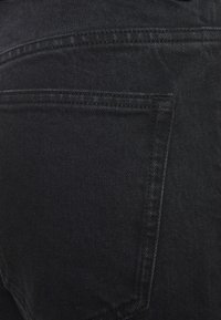 Gros plan d'une poche arrière sur un jean en denim noir, montrant les coutures détaillées et la texture du tissu.