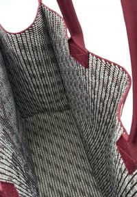 Dentro di una borsa in tessuto con una profonda bordatura bordeaux, che presenta un interno texturizzato e decorato con linee intrecciate grigie e nere.