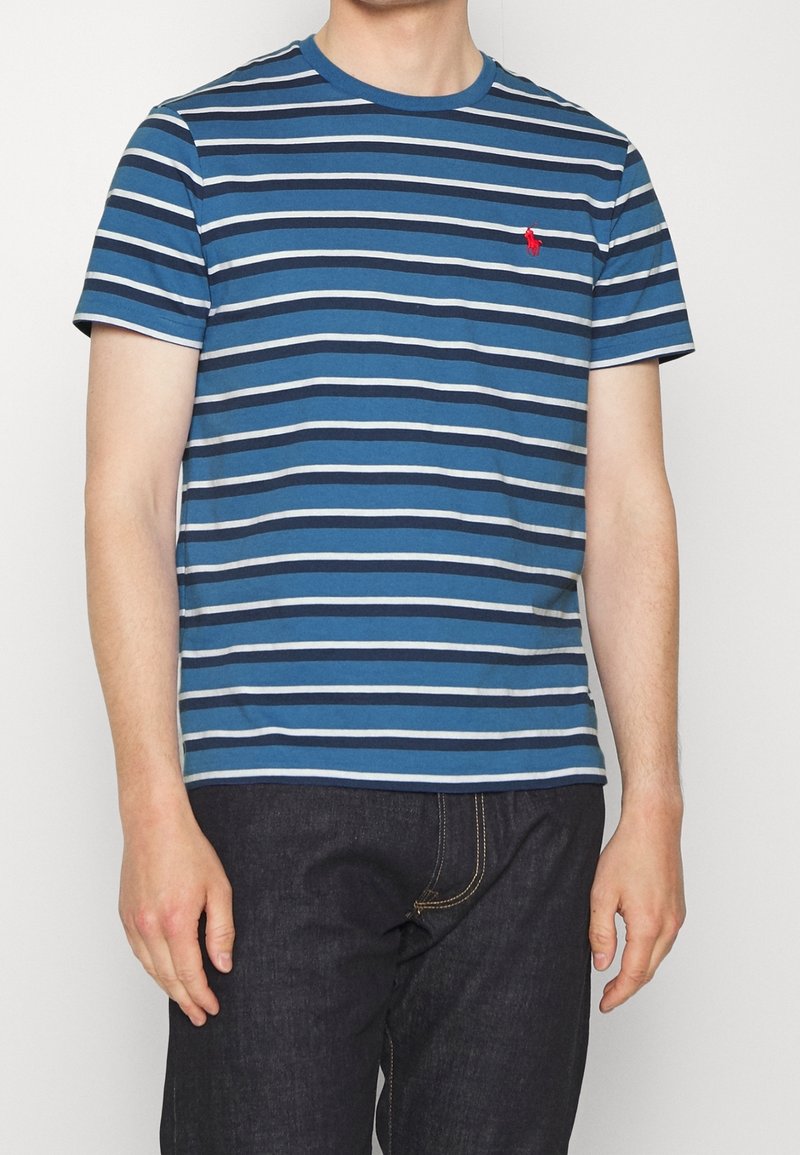 Blårandig t-shirt i bomull med horisontella ränder i olika nyanser av blått och grått. Har en röd logotyp på bröstet.