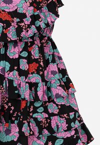 Černá látka s vrstvenými volány zdobenými květinovými vzory v růžové, fialové, zelené a červené barvě s malými listy a kvítky.