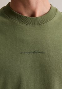 Bluza w oliwkowej zieleni z okrągłym, prążkowanym dekoltem oraz subtelnym, czarnym haftowanym logo na piersi, wykonana z mieszanki bawełny.