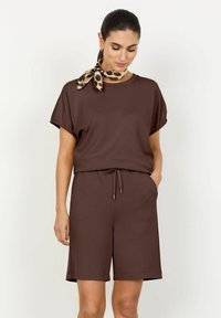 Completo a due pezzi marrone composto da un tessuto morbido. Presenta una parte superiore a vestibilità comoda con maniche arrotolate e pantaloni corti con coulisse, completato da una sciarpa con stampa leopardata.