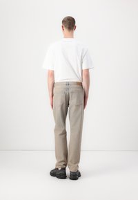 Maglietta bianca aderente e jeans beige a gamba dritta, con una toppa in pelle sul retro, cuciture a contrasto e sneaker nere.