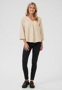 Blouse beige légère avec un col en V et des manches trois-quarts, associée à un jean slim noir et des mocassins noirs.