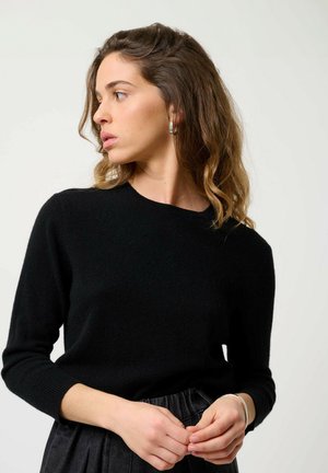 Schwarzer, gestrickter Pullover mit einem runden Ausschnitt und Dreiviertelärmeln, kombiniert mit einem schwarzen, plissierten Rock. Glatte Textur, figurbetontes Design.