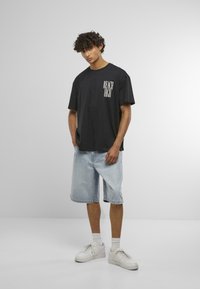 Black cotton t-shirt with "REACH HIGH" text in white, paired with light blue denim shorts and white sneakers with grey accents.