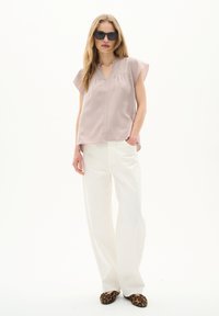 Top leggero viola con maniche a cappuccio e scollatura a V, abbinato a pantaloni bianchi larghi e scarpe flat con stampa leopardata. Texture liscia, stile moderno.