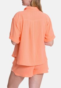 Kurzärmliges orangenes Hemd und passende Shorts aus leichtem, strukturiertem Stoff mit lockerem Schnitt und umgeschlagenen Ärmeln.