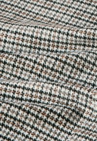 Vävt tyg med hounds-tooth mönster i svart, vitt och brunt. Mjuk textur med konsekvent detaljering genom hela materialet.