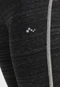 Czarne legginsy sportowe z szarymi paskami po bokach. Materiał ma melanżową fakturę. Na udzie znajduje się małe srebrne logo.