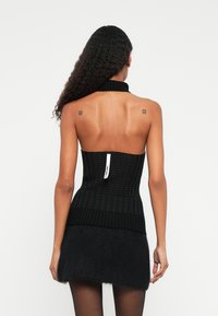 Černý pletený top s vysokým vroubkovaným límcem a texturovaným vzorem. Nosený s nadýchanou černou sukní, která má na zadní straně viditelnou etiketu.