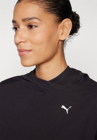 Svart hettegenser med glatt tekstur og en hvit Puma-logo på brystet. Designet har høy krage og minimalistisk stil.