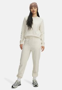 Crème kleurig sweatshirt en jogger set van zacht materiaal, met elastische boorden, een trekkoord in de taille, en gecombineerd met grijze sportieve sneakers.