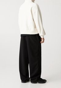 Weißer Fleece-Pullover mit hohem Kragen, lässiger Schnitt; kombiniert mit lockeren schwarzen Hosen und schwarzen Sportschuhen. Einfaches, minimalistisches Design.