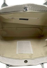 Lys grå håndtaske lavet af tekstureret læder med slangeskinds mønster, der har et rummeligt beige interiør og en lynlåslomme.