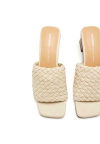 Sandalias de plataforma beige con parte superior trenzada, punta cuadrada y tacón bajo. Textura de cuero suave con un diseño minimalista.