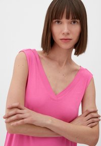 Różowy bezrękawnik z dekoltem w kształcie litery V, wykonany z miękkiego materiału. Posiada gładką strukturę i prosty krój, bez wzorów ani akcentów.