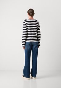 Stripete langermet skjorte i svart og hvitt, med rund hals, kombinert med løstsittende blå denim jeans og uformelle hvite joggesko.