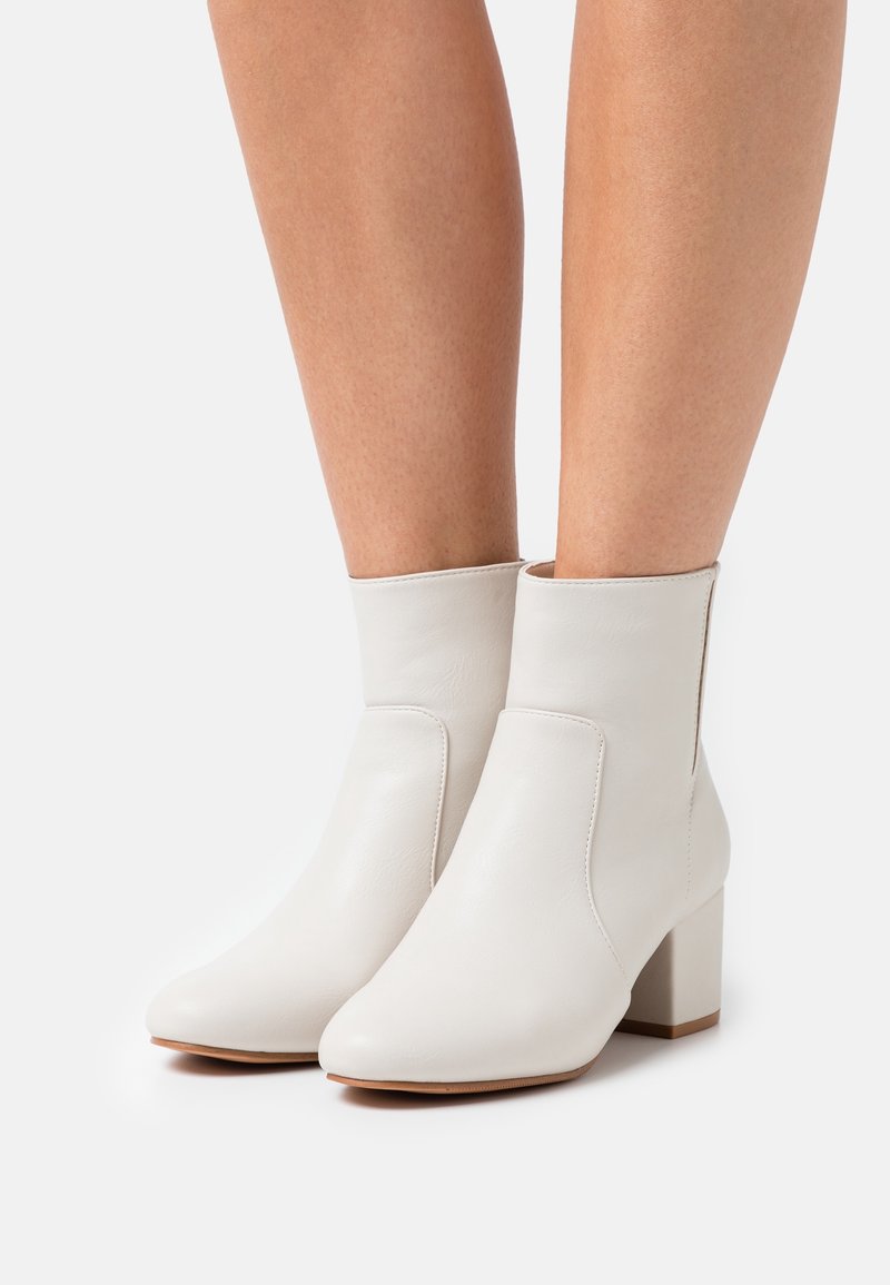 Białe skórzane botki za kostkę na słupku, z ostrym noskiem i minimalnym przeszyciem z boku. Gładka tekstura i prosty design.