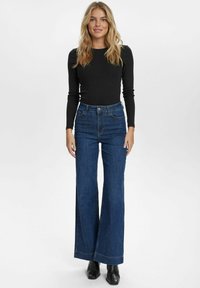 High-waisted, wide-leg blue denim jeans with a classic five-pocket design and subtle stitching details. Paired with a fitted black long-sleeve top.