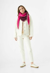 Veste en denim crème sur un haut beige, jeans blancs et baskets légères. Écharpe rose et bordeaux avec des coutures contrastées.