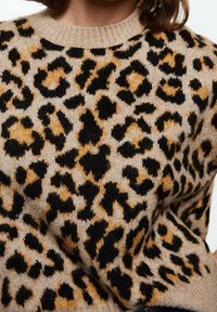 Pull beige avec imprimé léopard noir et or. Texture douce, col côtelé ; le motif présente des formes et des tailles variées.