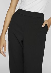 Črne široke hlače iz gladkega materiala. Imajo visok pas in stranske žepe. Očitno šivanje obkroža sprednji del.