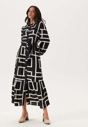 Robe longue noire et blanche à motif avec un devant boutonné, une taille cintrée, des manches bouffantes et une jupe à volants. Convient à diverses occasions.