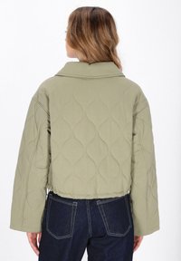 Giacca cropped trapuntata verde oliva con maniche oversize, caratterizzata da una colletto a costine e una texture liscia. Vengono indossati jeans in denim blu.