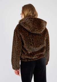 Brązowa kurtka z sztucznego futra z wzorem w panterkę, dużym kapturem i luźnym krojem, w połączeniu z czarnymi spodniami z korduroy.