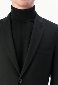 Black suit jacket with a slim fit, featuring a notch lapel, single button closure, and a black turtleneck underneath. Smooth texture.