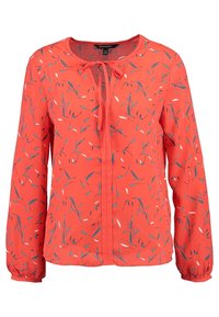 Röd blus med blommönster som har blåa och vita blad, långa ärmar, rund halsringning och en knytning fram.