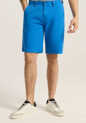 Niebieskie bawełniane szorty o prostym kroju, z zapięciem na guzik z przodu oraz kieszeniami. W połączeniu z białymi i granatowymi sneakersami.